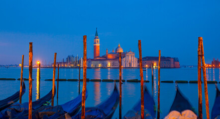 View of San Giorgio Island in Venice with wooden buoys in Giudecca Canal  at twilight blue hour - Venetian gondolier  - obrazy, fototapety, plakaty