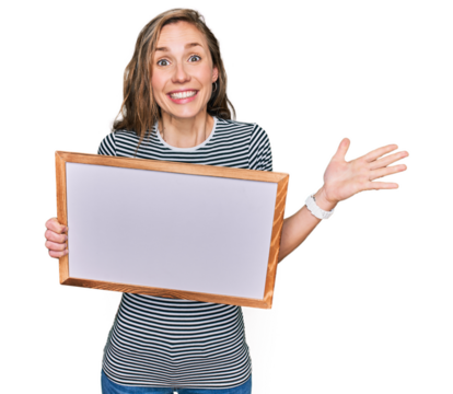 Young blonde woman holding empty white board celebrating victory with happy smile and winner expression with raised hands