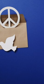 Vertical video of white dove with leaf, white peace sign, envelope and copy space on blue background