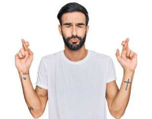 Young hispanic man wearing casual white t shirt gesturing finger crossed smiling with hope and eyes closed. luck and superstitious concept.