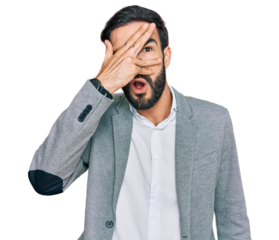 Young hispanic man wearing business clothes peeking in shock covering face and eyes with hand, looking through fingers with embarrassed expression.