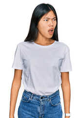 Beautiful young asian woman wearing casual white t shirt angry and mad screaming frustrated and furious, shouting with anger. rage and aggressive concept.