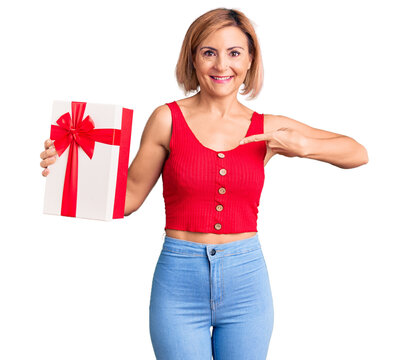 Young blonde woman holding gift pointing finger to one self smiling happy and proud