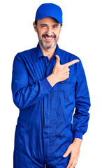 Middle age handsome man wearing mechanic uniform cheerful with a smile on face pointing with hand and finger up to the side with happy and natural expression