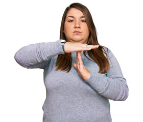 Beautiful brunette plus size woman wearing casual clothes doing time out gesture with hands,...