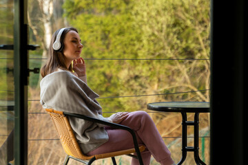 Relaxed woman with headphones breathes fresh air, meditates, listens to music on the terrace at...