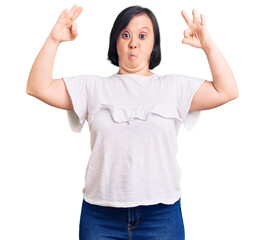 Brunette woman with down syndrome wearing casual white tshirt looking surprised and shocked doing ok approval symbol with fingers. crazy expression