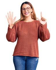 Beautiful young woman wearing casual clothes and glasses showing and pointing up with fingers number seven while smiling confident and happy.