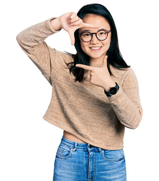 Young chinese woman wearing casual sweater and glasses smiling making frame with hands and fingers with happy face. creativity and photography concept.