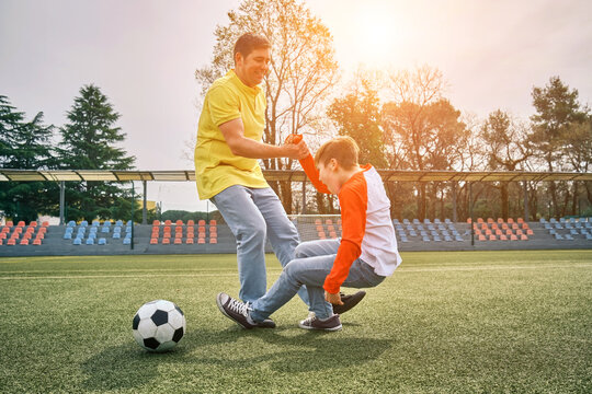 Father and Son play football on stadium outdoors, Happy family bonding, fun, players in soccer in dynamic action playing in sunny day, holidays time.
