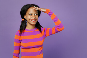 Little kid teen girl of African American ethnicity 15-16 years old wear orange sweatshirt hold hand at forehead look far away distance isolated on plain purple background. Childhood lifestyle concept.