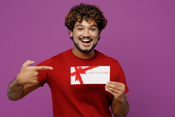 Young happy Indian man he wears red t-shirt casual clothes hold point finger on gift certificate...