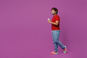 Full body side view young Indian man he wear red t-shirt casual clothes hold takeaway delivery craft paper brown cup coffee to go isolated on plain purple background studio portrait Lifestyle concept