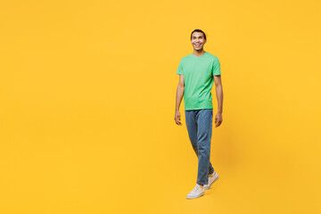 Fototapeta na wymiar Full body smiling happy cheerful young man of African American ethnicity he wears casual clothes green t-shirt hat walking going isolated on plain yellow background studio portrait. Lifestyle concept.
