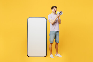 Full body young promoter man he wear light purple t-shirt casual clothes big huge blank screen mobile cell phone smartphone with area scream hot news in megaphone isolated on plain yellow background.