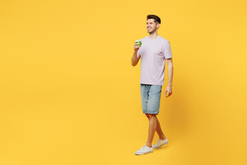 Fototapeta na wymiar Full body young man he wear light purple t-shirt casual clothes hold takeaway delivery craft paper brown cup coffee to go walk isolated on plain yellow background studio portrait. Lifestyle concept.