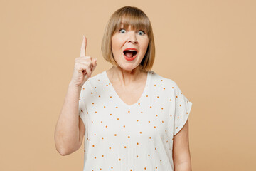 Proactive blonde elderly woman 50s years old wear casual clothes holding index finger up with great new idea isolated on plain pastel light beige color background studio portrait. Lifestyle concept.