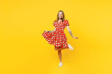 Full body young smiling cheerful fun cool happy caucasian woman she wearing red dress casual clothes looking camera rasie up leg isolated on plain yellow background studio portrait. Lifestyle concept.