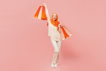 Full body happy young arabian asian muslim woman wearing orange abaya hijab hold shopping package...