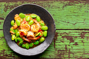 Pad Ped Sator Goong, Thai food, Shrimps and Stink Beans Fried in Red Curry Paste in wabi sabi plate on green wood texture background, top view, Pakria, Bitter bean, Twisted cluster bean, Stink bean