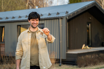 Young smiling man showing keys to new home. Real estate, apartment and people concept. 