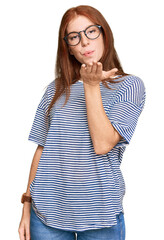 Young read head woman wearing casual clothes and glasses looking at the camera blowing a kiss with hand on air being lovely and sexy. love expression.