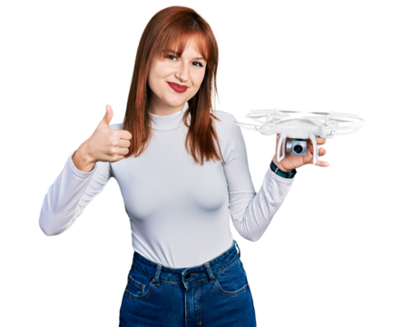 Redhead young woman holding drone smiling happy and positive, thumb up doing excellent and approval sign