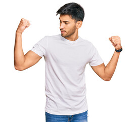 Young handsome man wearing casual white tshirt showing arms muscles smiling proud. fitness concept.
