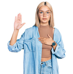 Beautiful young blonde woman wearing glasses swearing with hand on chest and open palm, making a...