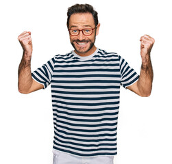 Fototapeta premium Middle age man wearing casual clothes and glasses celebrating surprised and amazed for success with arms raised and open eyes. winner concept.