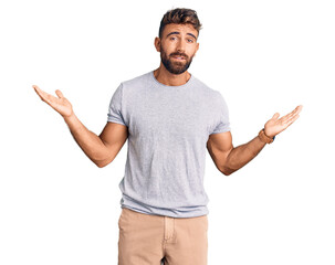Young hispanic man wearing casual clothes clueless and confused expression with arms and hands...