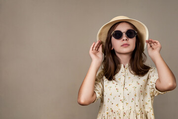 Portrait of little girl in retro image with sunglasses, hat and summer wear posing at grey, pensive looking. Stylish lovely kid lady with positive emotion. Fashion style concept. Copy ad text space