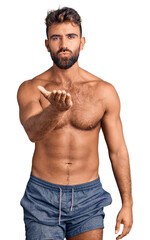 Young hispanic man wearing swimwear shirtless looking at the camera blowing a kiss with hand on air...