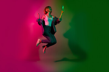 Fototapeta na wymiar Full length photo of positive lady jump raise fist up winning discount on smart phone disco club on vivid neon color background