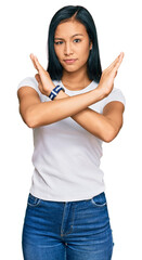 Beautiful hispanic woman wearing casual white tshirt rejection expression crossing arms doing negative sign, angry face