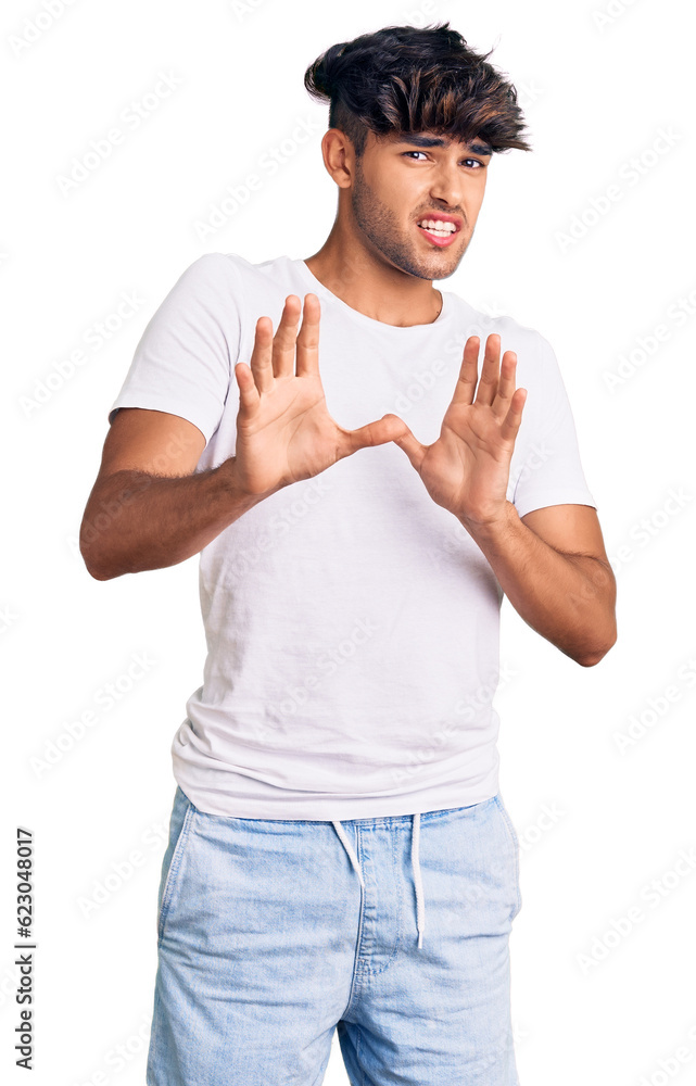 Wall mural Young hispanic man wearing casual clothes disgusted expression, displeased and fearful doing disgust face because aversion reaction. with hands raised