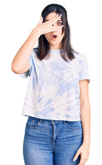Fototapeta premium Young beautiful girl wearing casual t shirt peeking in shock covering face and eyes with hand, looking through fingers with embarrassed expression.