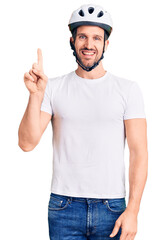 Young handsome man wearing bike helmet showing and pointing up with finger number one while smiling confident and happy.