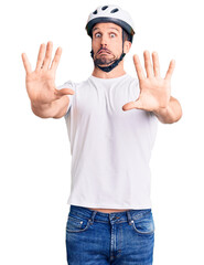 Young handsome man wearing bike helmet afraid and terrified with fear expression stop gesture with hands, shouting in shock. panic concept.