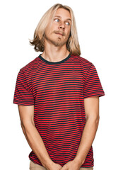 Caucasian man with blond long hair wearing casual striped t shirt smiling looking to the side and staring away thinking.