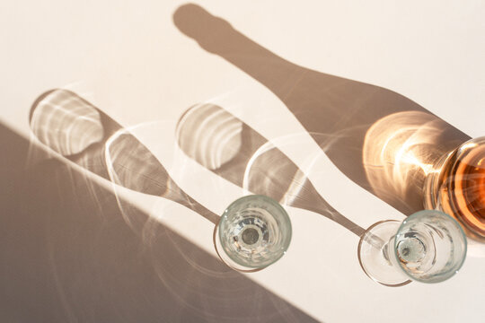 Different glasses for wine, cocktails, drinks, long sun shadow on a light beige background. The concept of wine tasting or summer vacation.