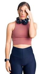 Beautiful caucasian young woman wearing gym clothes and using headphones worried and stressed about a problem with hand on forehead, nervous and anxious for crisis