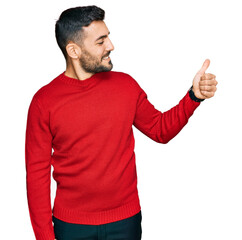 Young hispanic man wearing casual clothes looking proud, smiling doing thumbs up gesture to the side