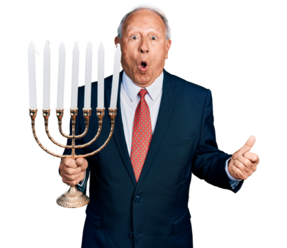 Senior business man with grey hair holding menorah hanukkah jewish candle scared and amazed with open mouth for surprise, disbelief face - Powered by Adobe