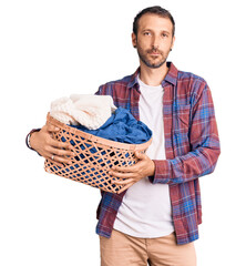 Young handsome man holding laundry basket thinking attitude and sober expression looking self...