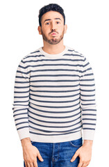 Obraz premium Young hispanic man wearing casual clothes puffing cheeks with funny face. mouth inflated with air, crazy expression.