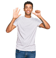 Young handsome african american man wearing casual white tshirt showing and pointing up with fingers number six while smiling confident and happy.