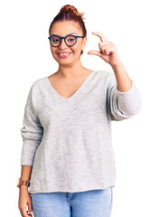 Young latin woman wearing casual clothes smiling and confident gesturing with hand doing small size sign with fingers looking and the camera. measure concept.