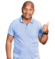 Hispanic middle age man wearing casual t shirt smiling with happy face looking and pointing to the side with thumb up.