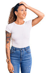 Young hispanic woman with tattoo wearing casual white tshirt smiling confident touching hair with hand up gesture, posing attractive and fashionable